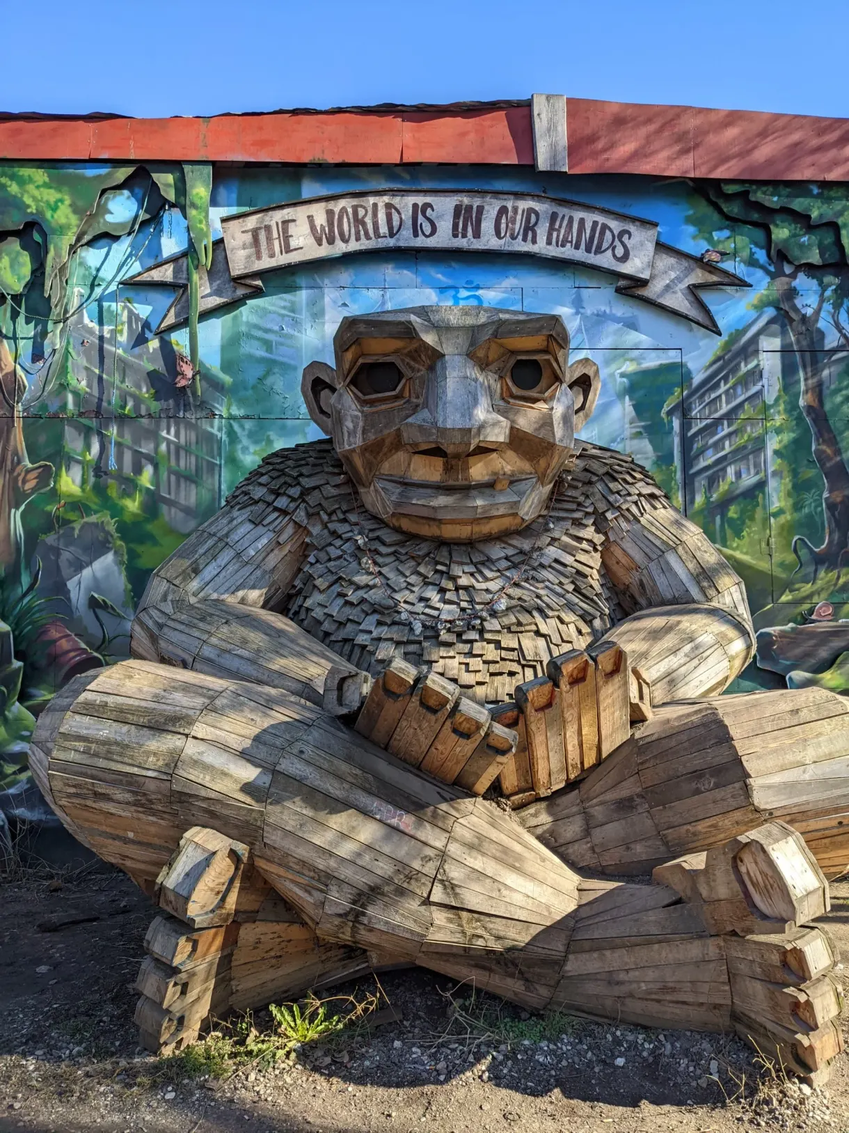 Troll géant en bois assis devant une fresque murale colorée