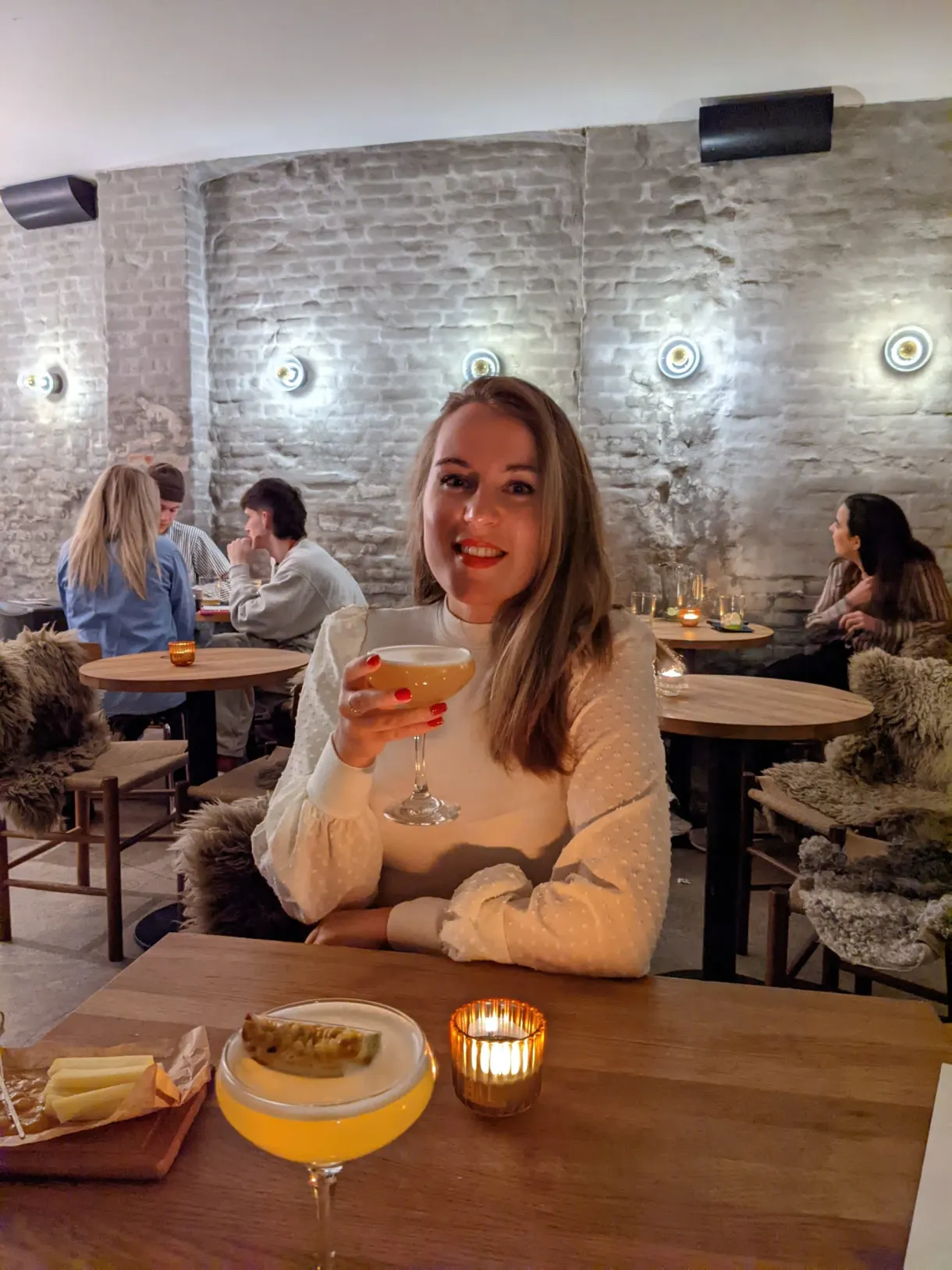 Voyageuse attablée levant son verre dans un café aux murs de brique