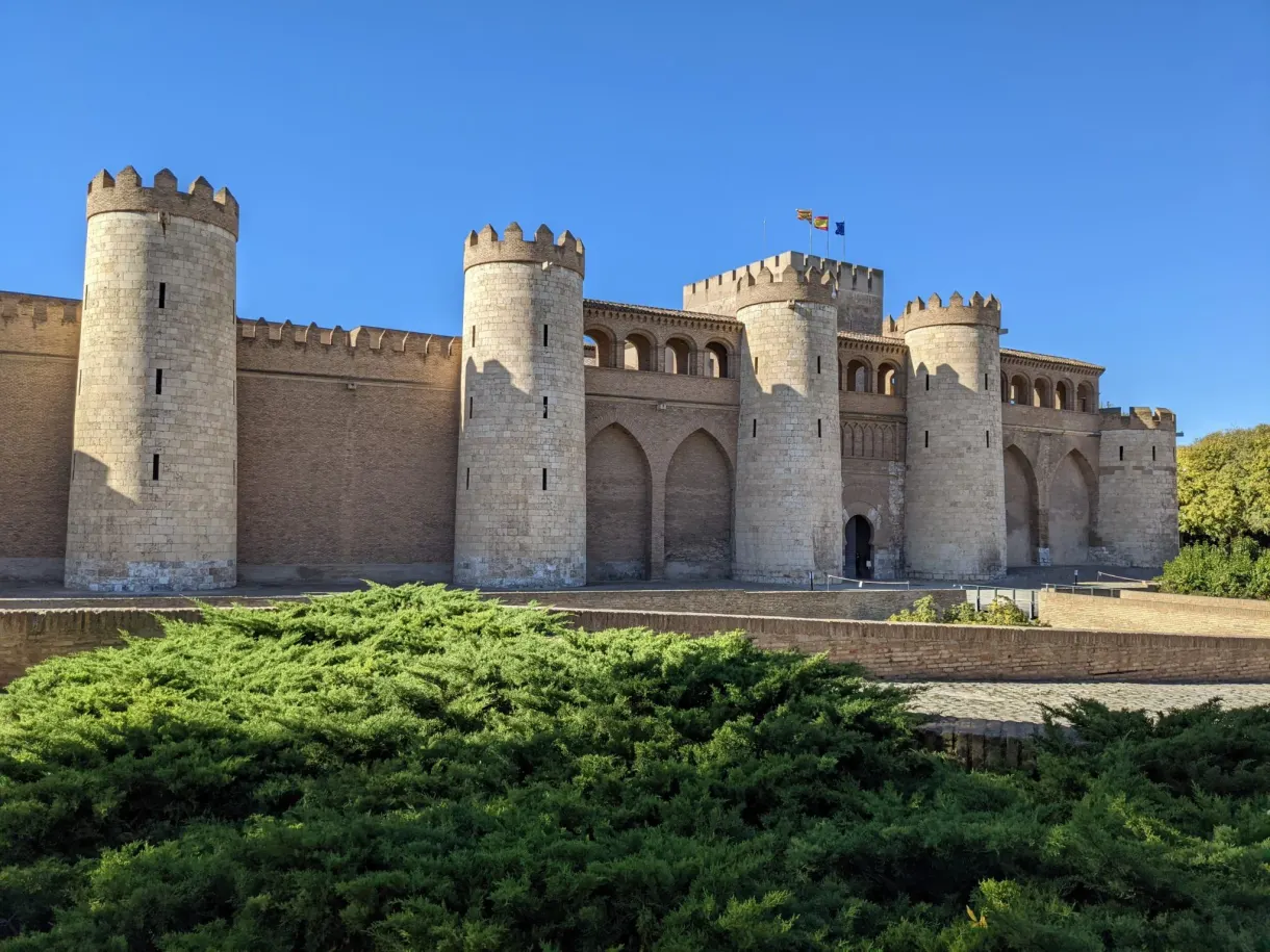 Crenellated walls of the Aljafería above the hedges