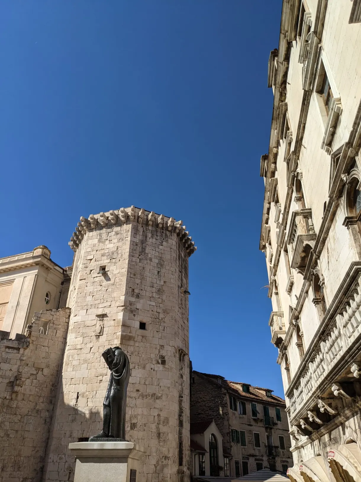 Square stone tower seen from below between two facades