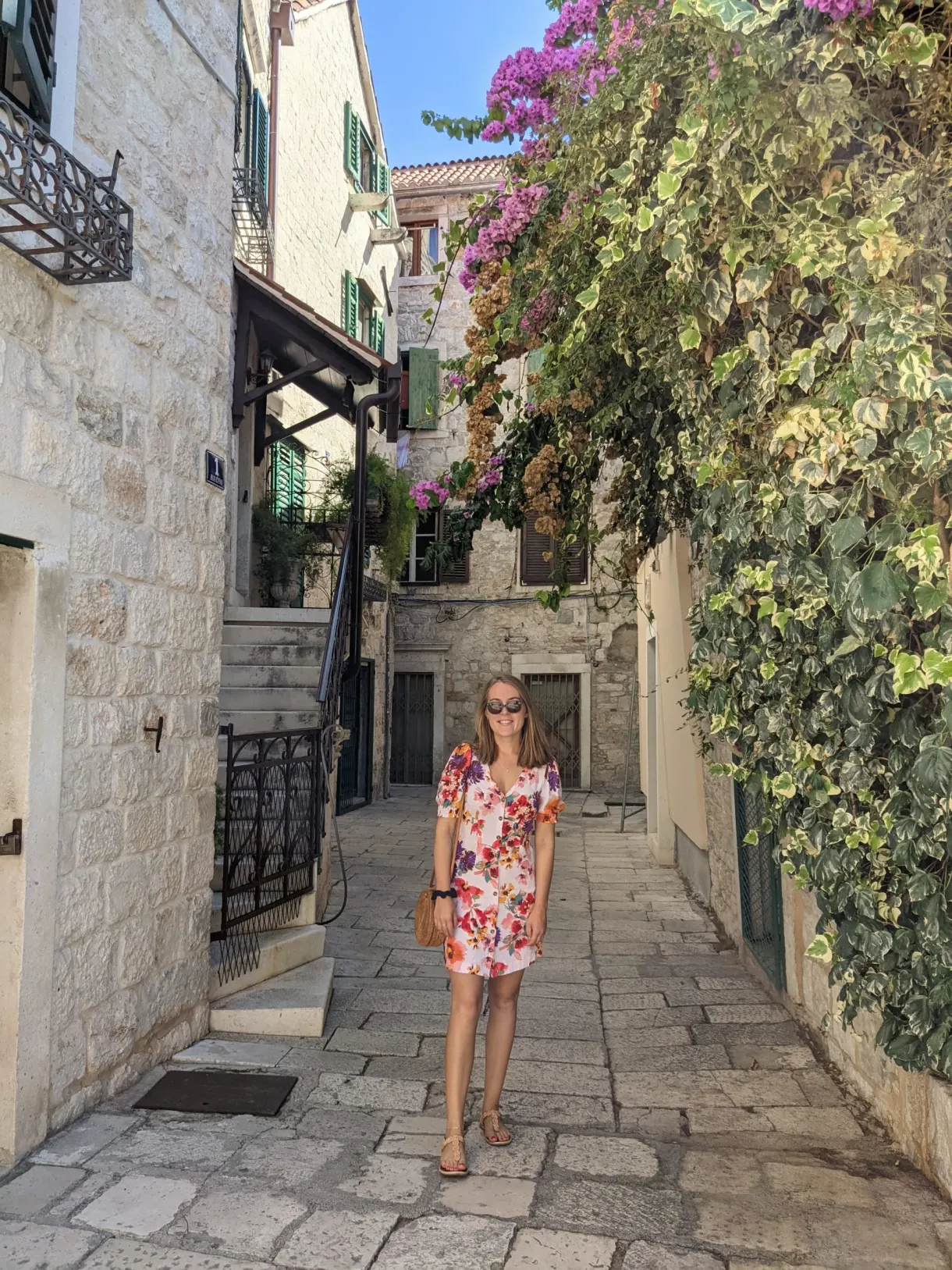 Woman in a floral dress in a cobbled lane lined with bougainvillea