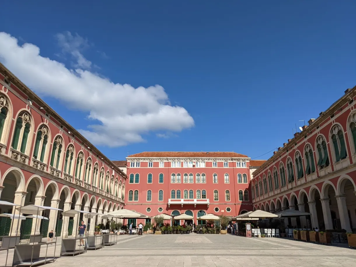 Large square lined with red arcades under a blue sky