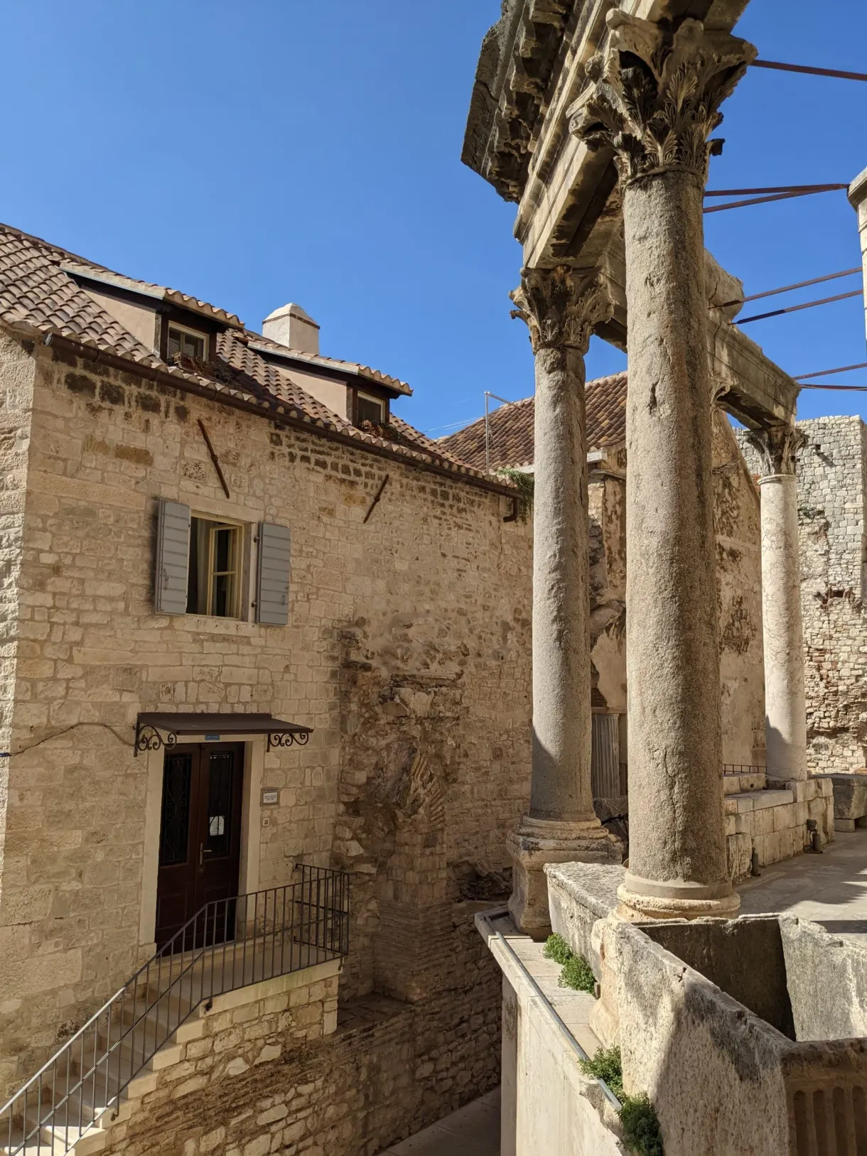 Ancient columns in front of a stone house with shutters