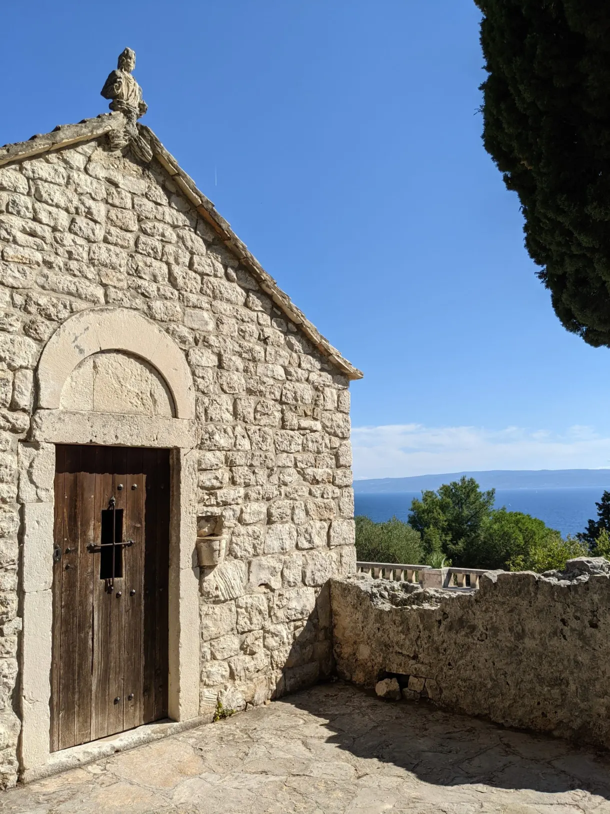 Small stone chapel with a wooden door and cypresses