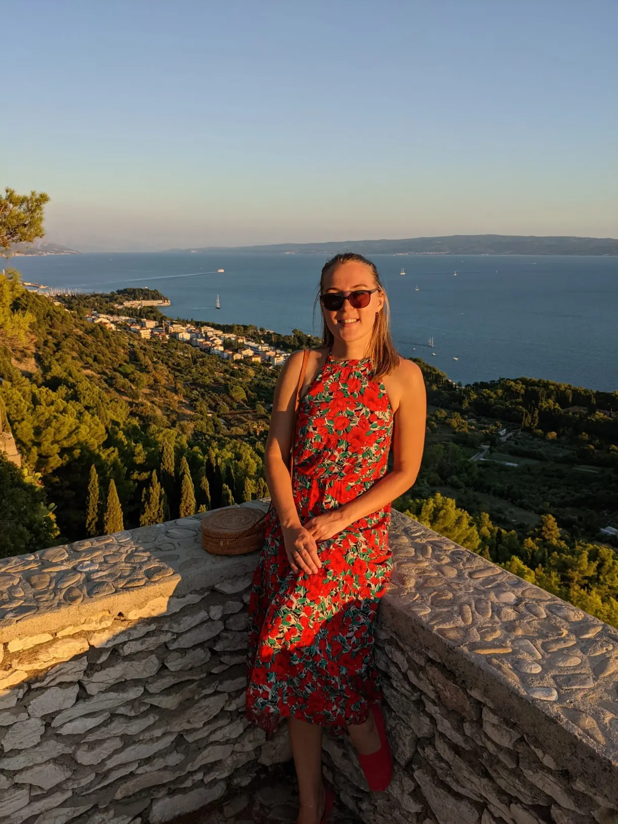 Woman in a floral dress sitting on a low wall facing the open sea