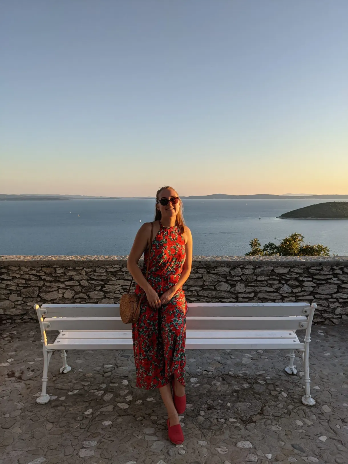 Woman standing in front of a white bench and a stone wall