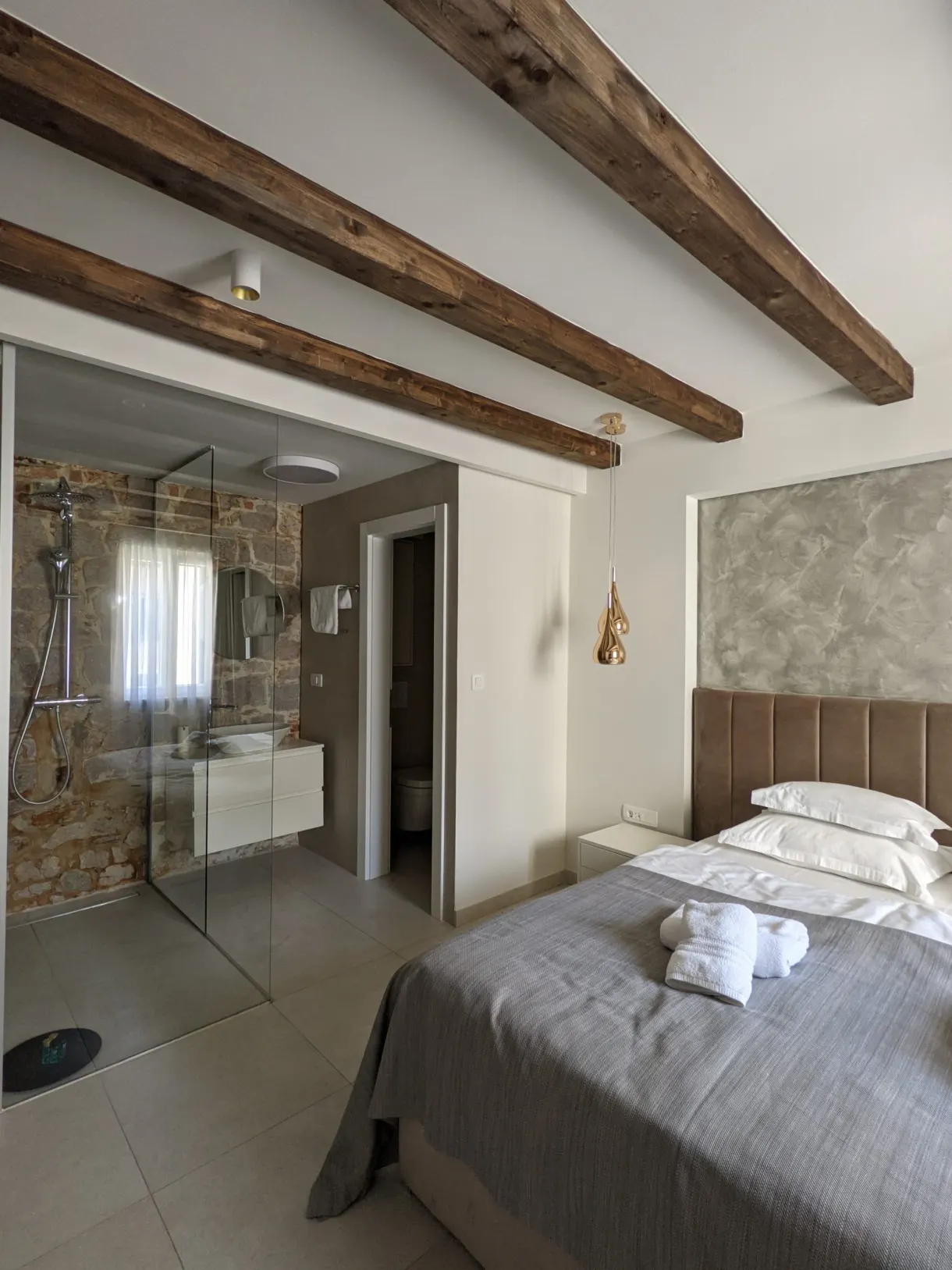 Room with exposed beams, a white bed and a glass shower