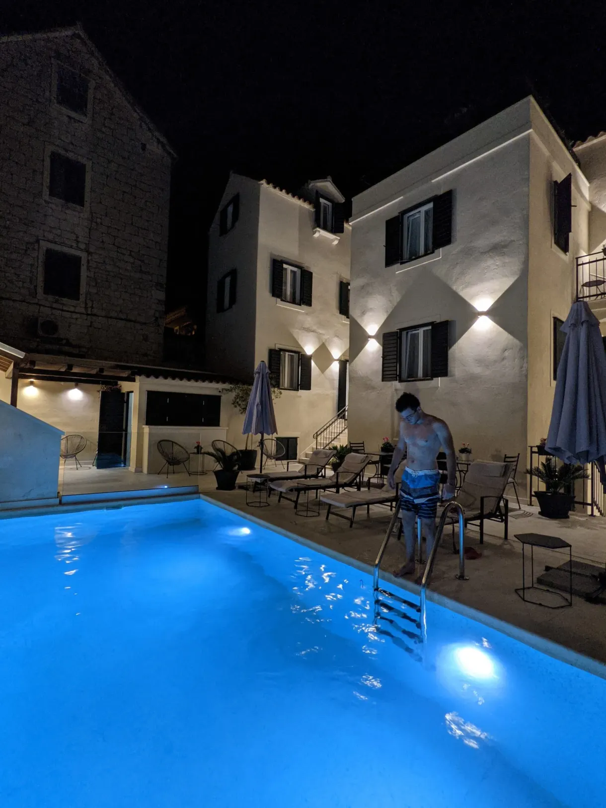 Man stepping into an illuminated blue pool in the evening