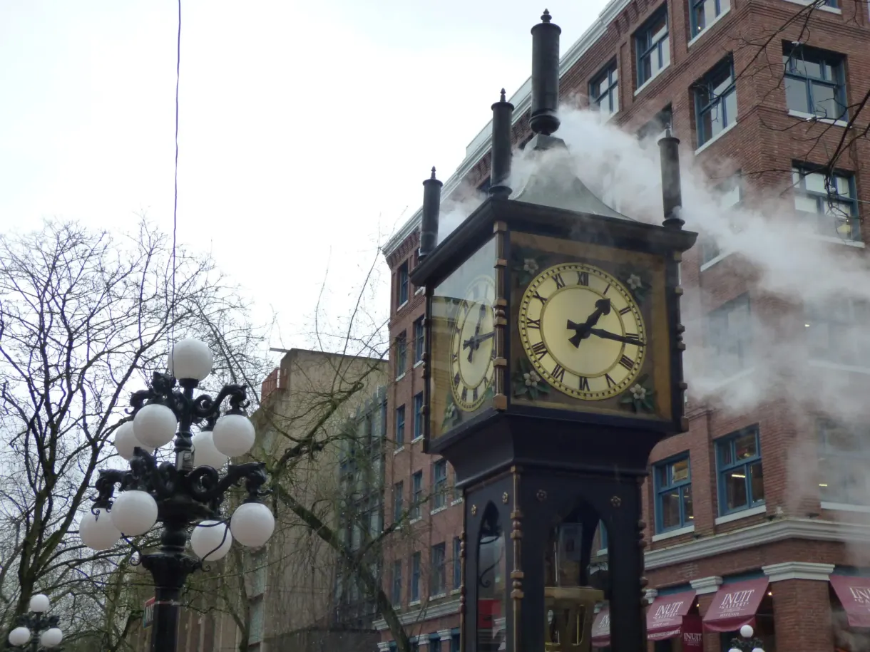 Steam clock puffing out its plume between the brick façades