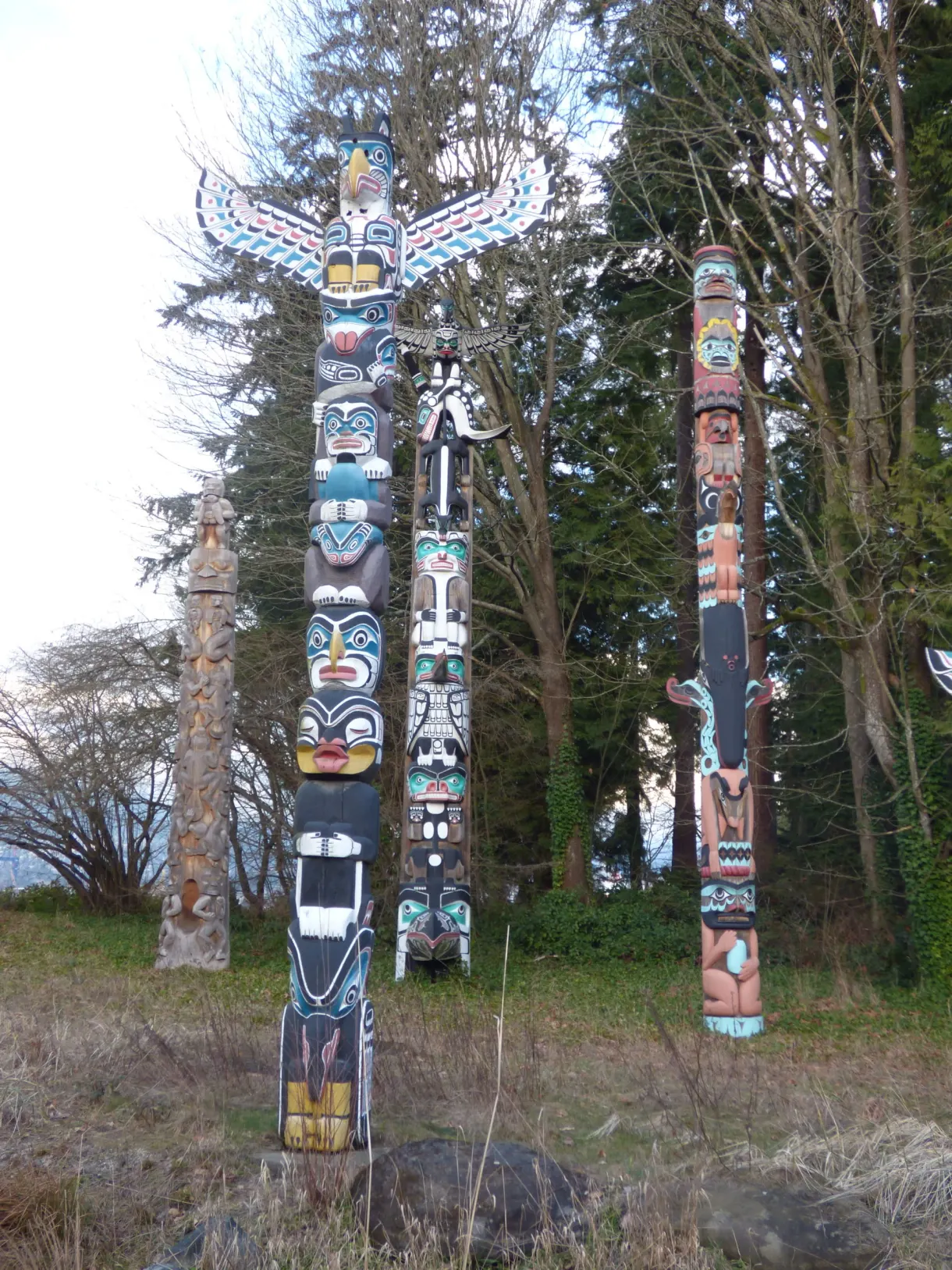 Row of painted totem poles in front of the fir trees
