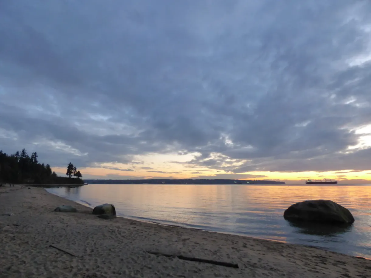 Sand and large pebbles at dusk facing the cargo ships