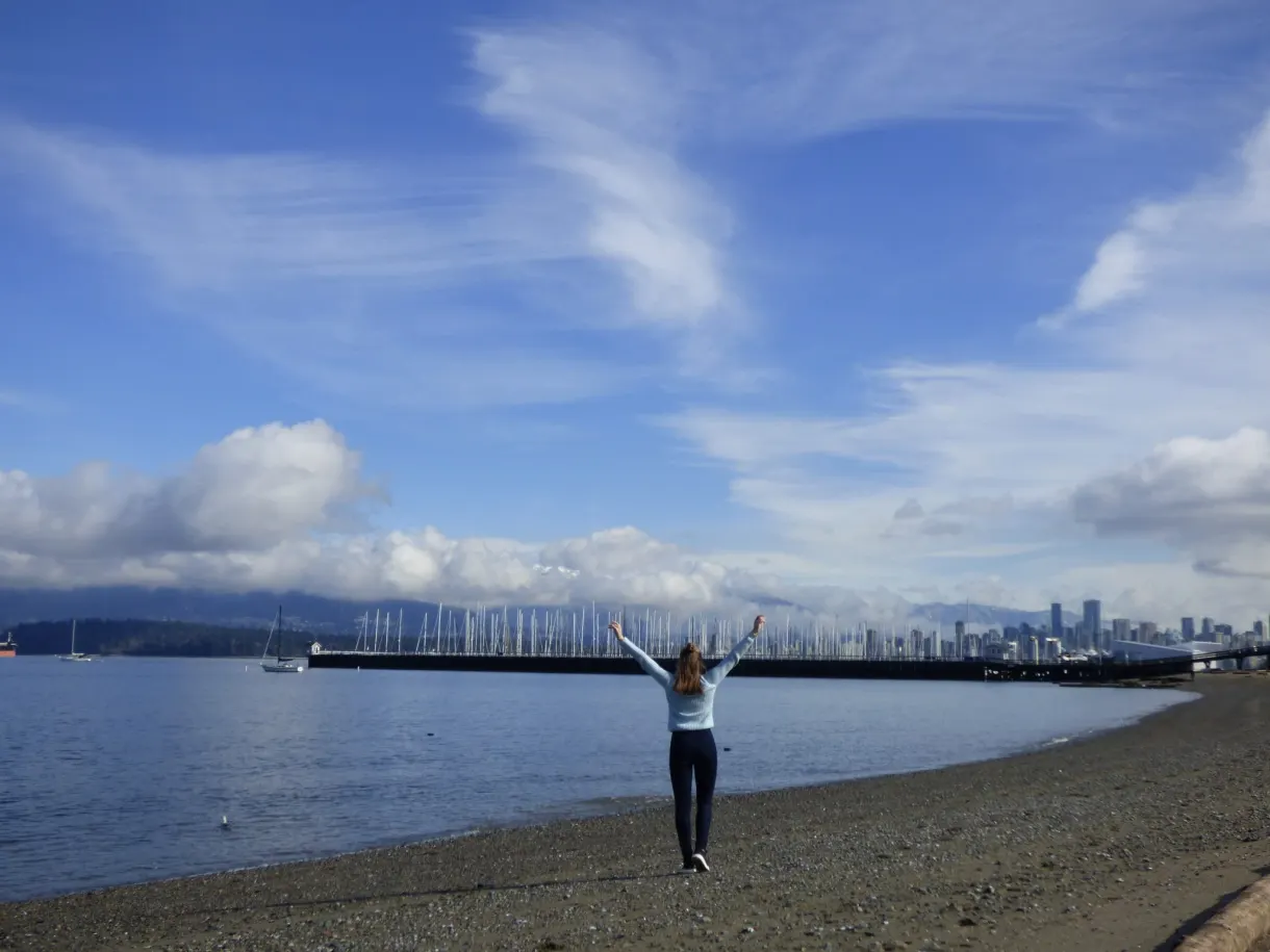 Arms raised on the beach under a sky of cirrus clouds