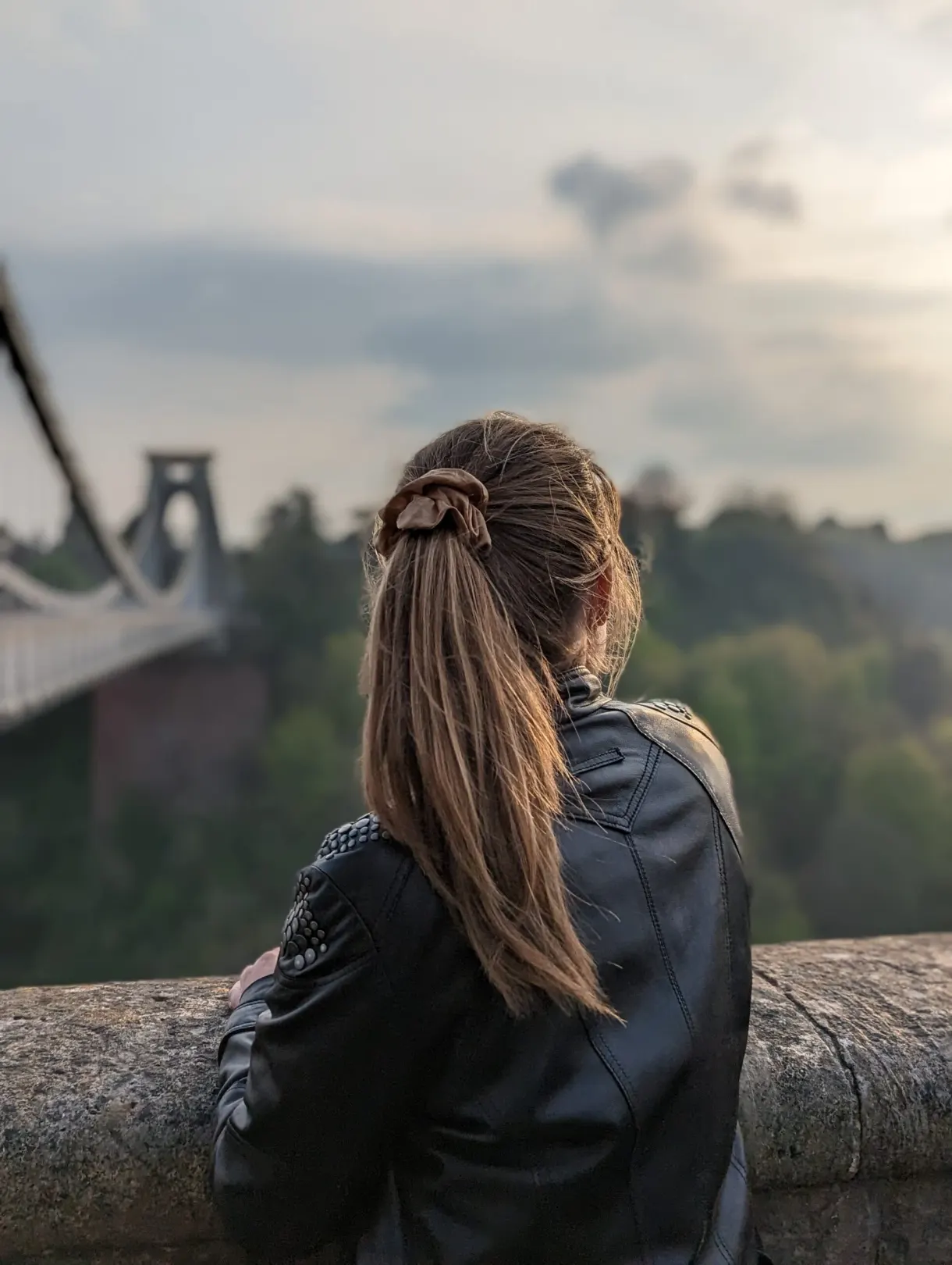 Seen from behind at the parapet, suspension bridge blurred behind