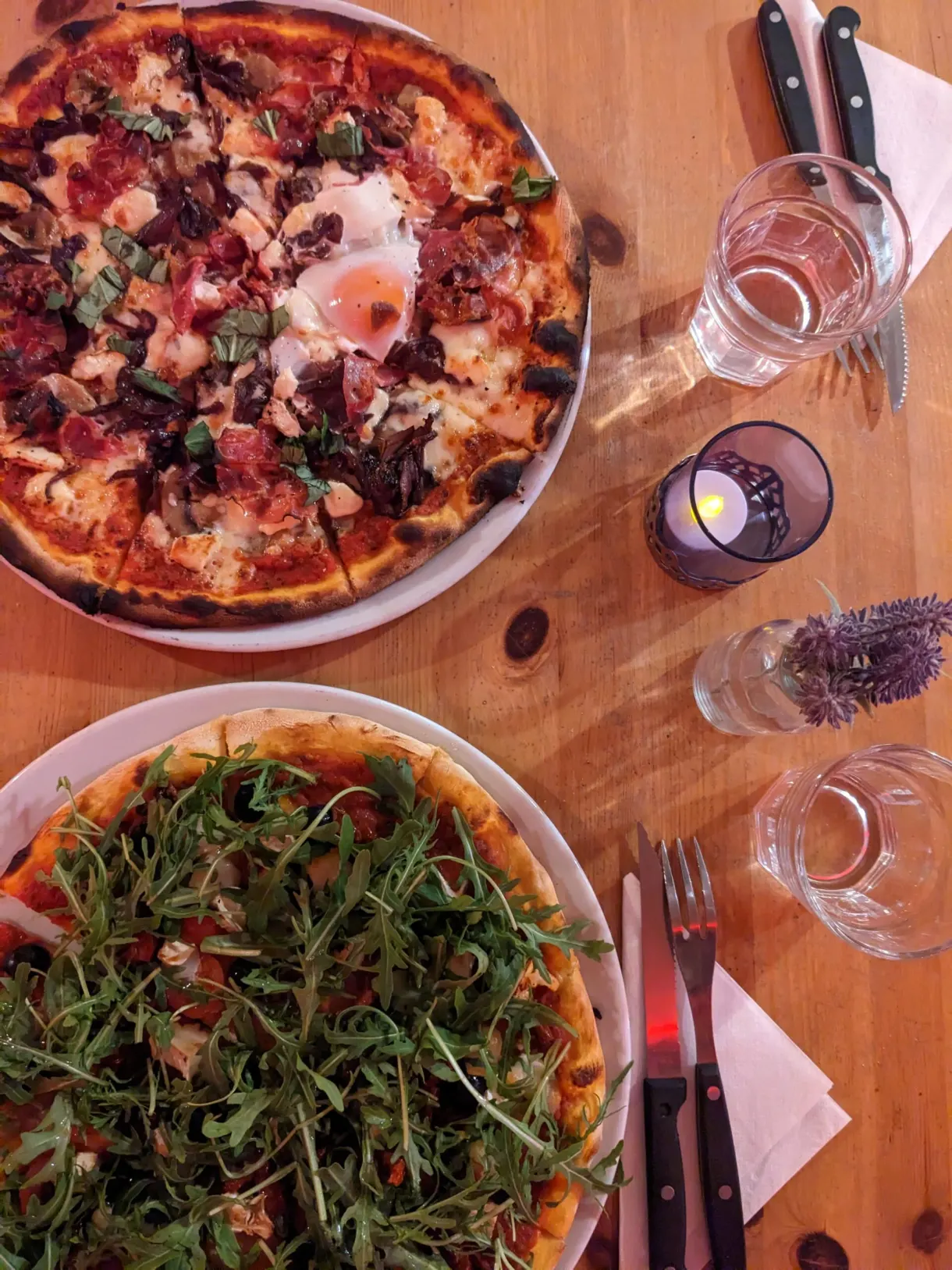 Two topped pizzas served on a wooden table