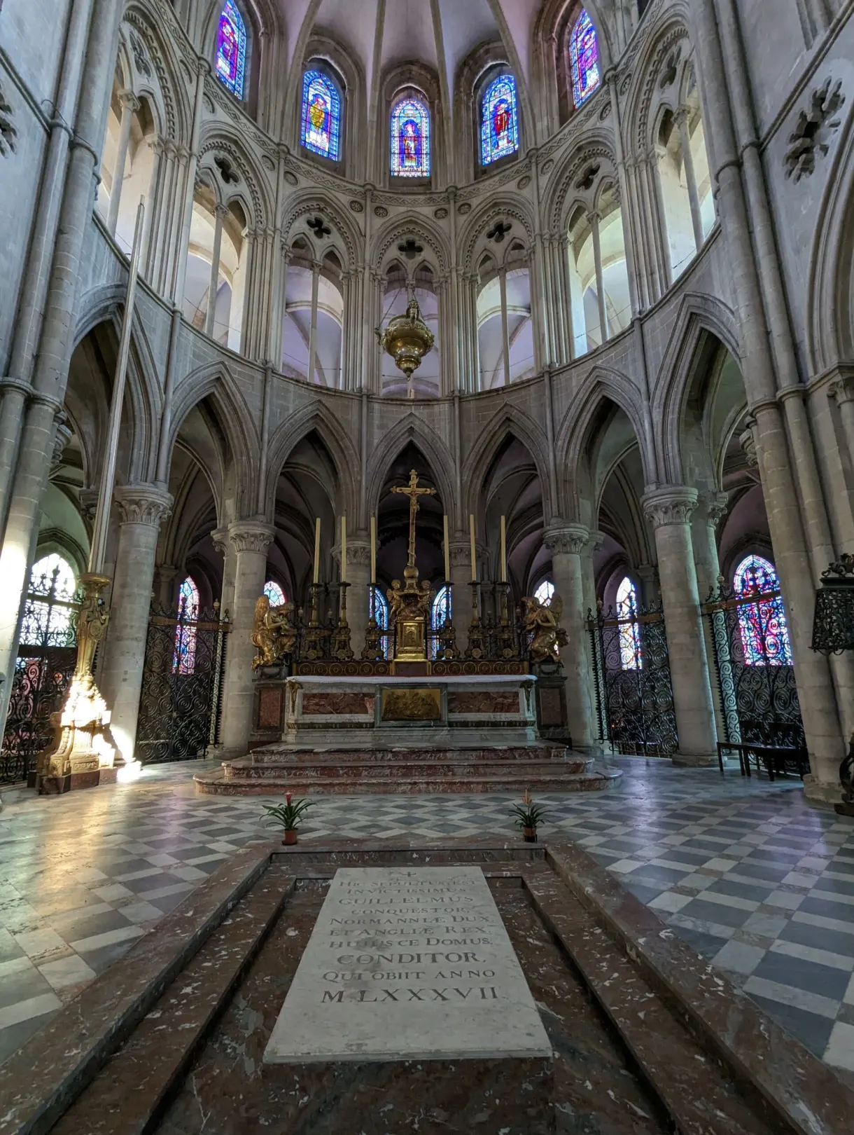 Choir with coloured stained glass and a funerary slab in the middle of the paving
