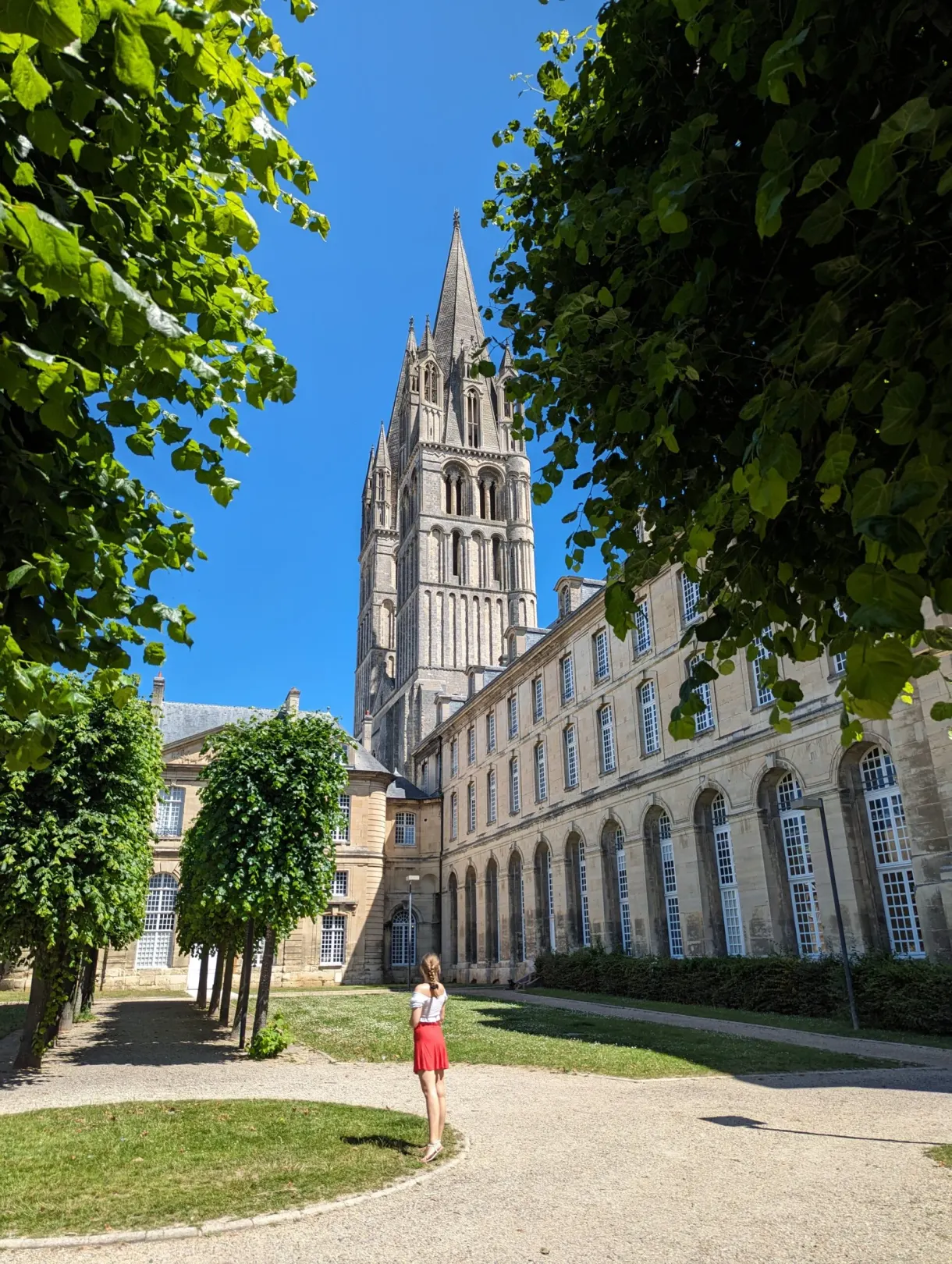 Avenue of clipped trees along the abbey, woman walking in a red dress