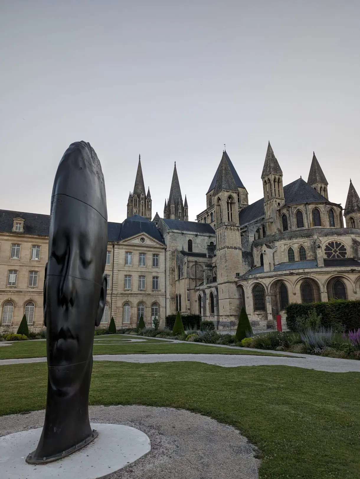 Black sculpture in the shape of an elongated face set in the garden