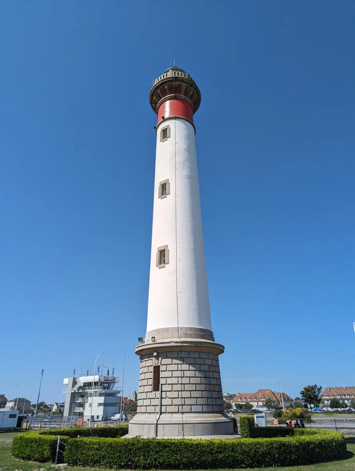 White lighthouse with a red crown overlooking the harbour of Ouistreham