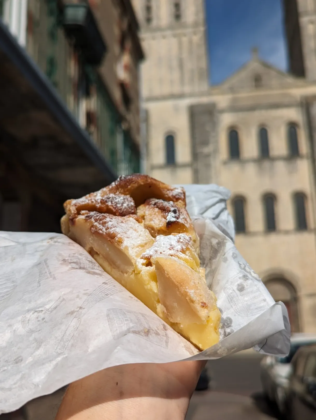 Slice of apple tart held in the hand in front of the abbey church
