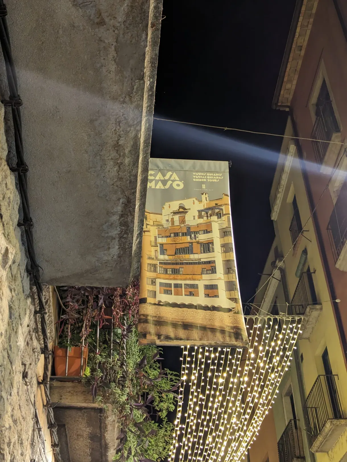 Casa Masó banner stretched above a lane lit with fairy lights