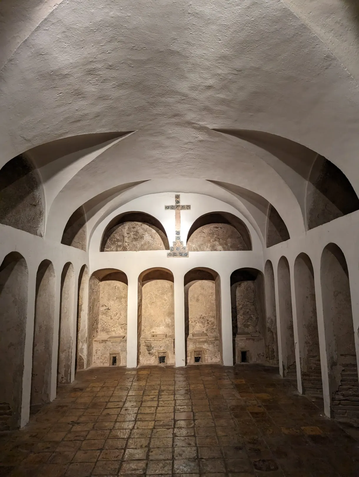 Whitewashed vaulted room with arched niches and a wall cross
