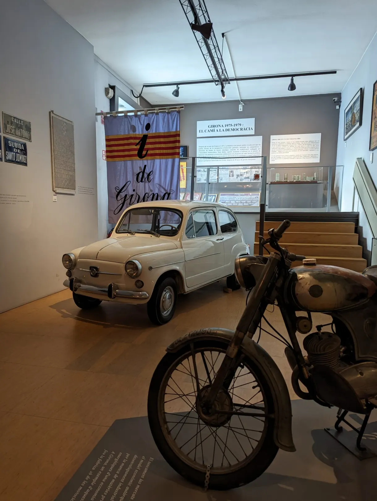 Small white vintage car and motorbike in front of a Catalan flag