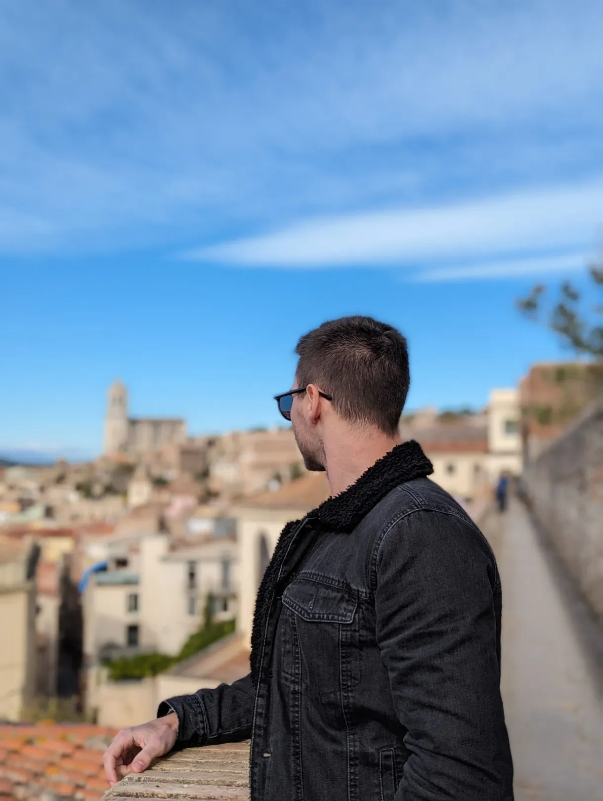 Man in profile leaning on the parapet in front of the roofs of Girona