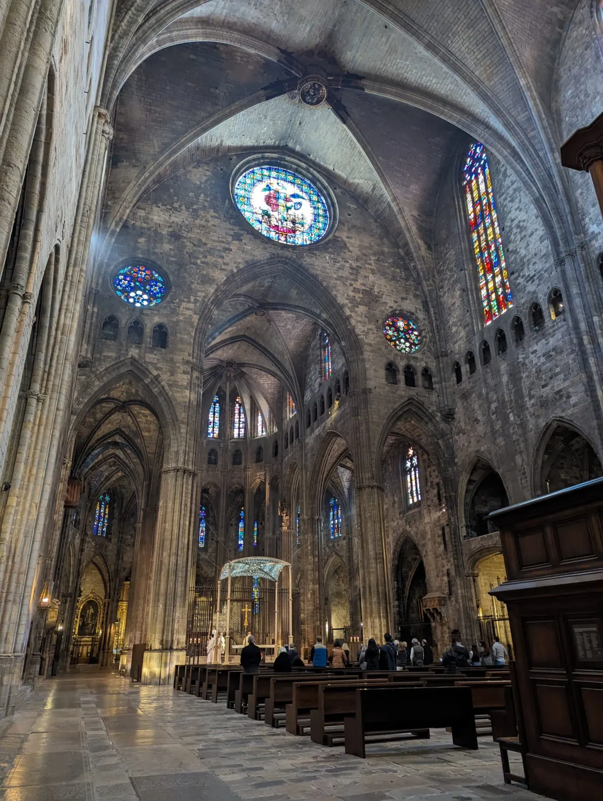 Gothic nave with rose windows and coloured stained glass, worshippers seated