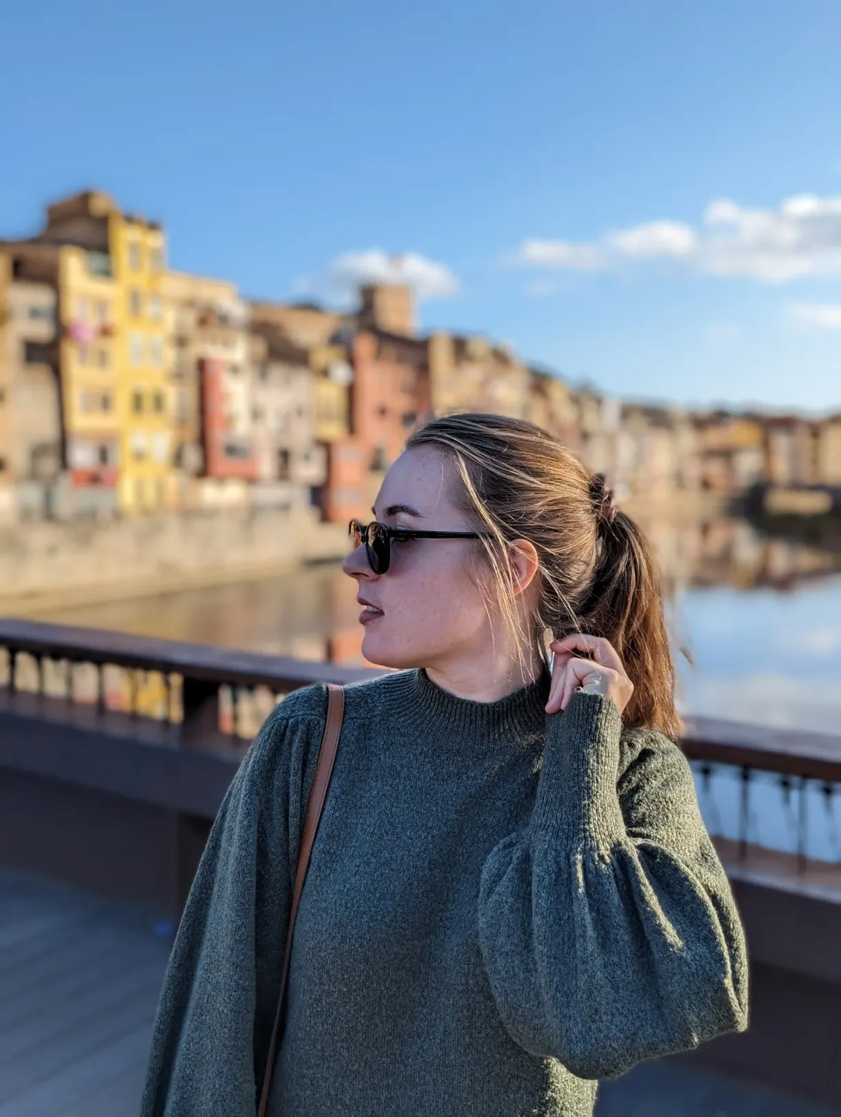 Woman in a green jumper on a bridge, colourful houses behind her