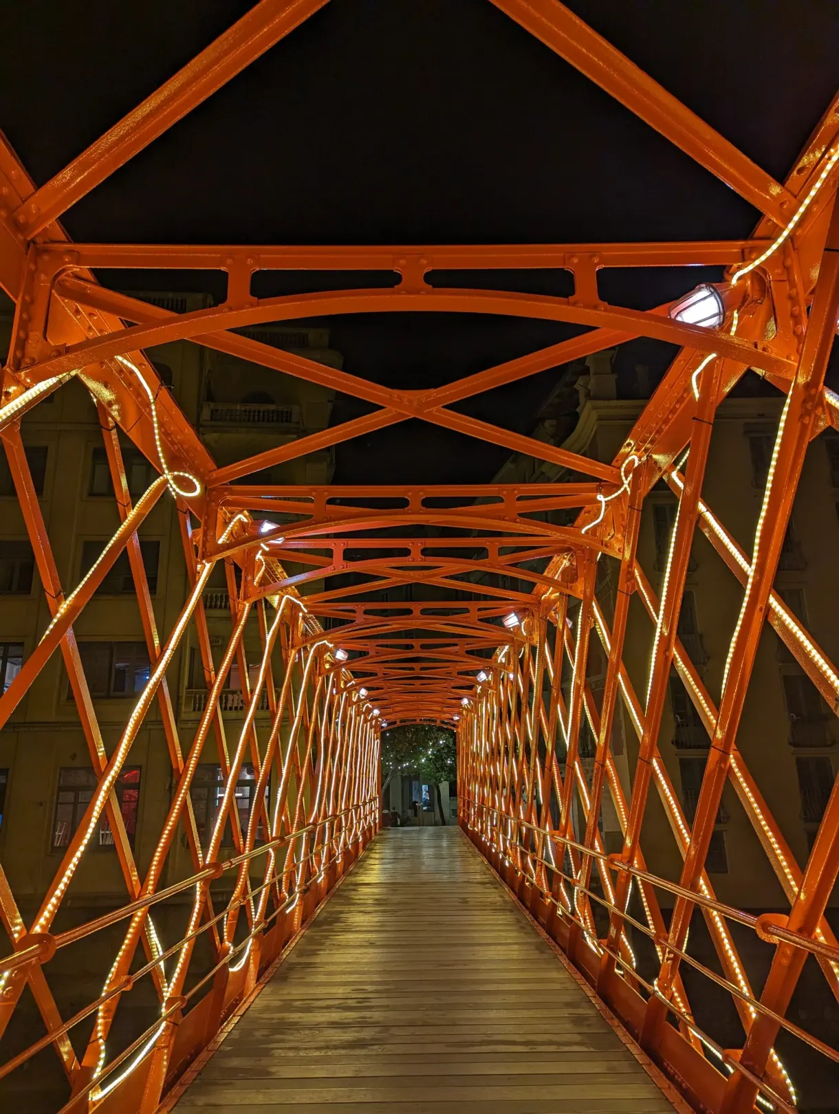 Orange metal footbridge lit from within after nightfall