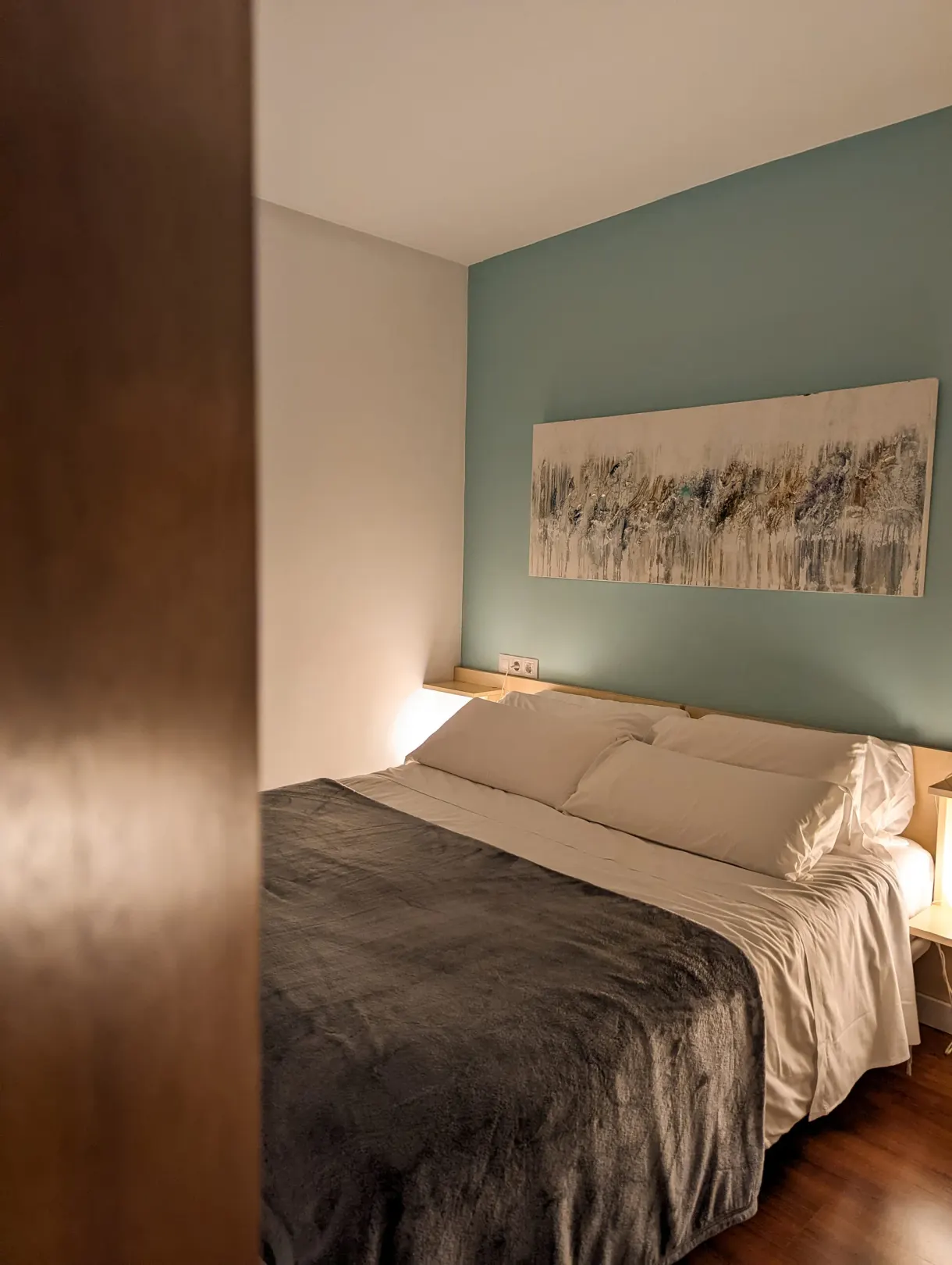 Bedroom with a sea green wall and a large bed covered with a blanket
