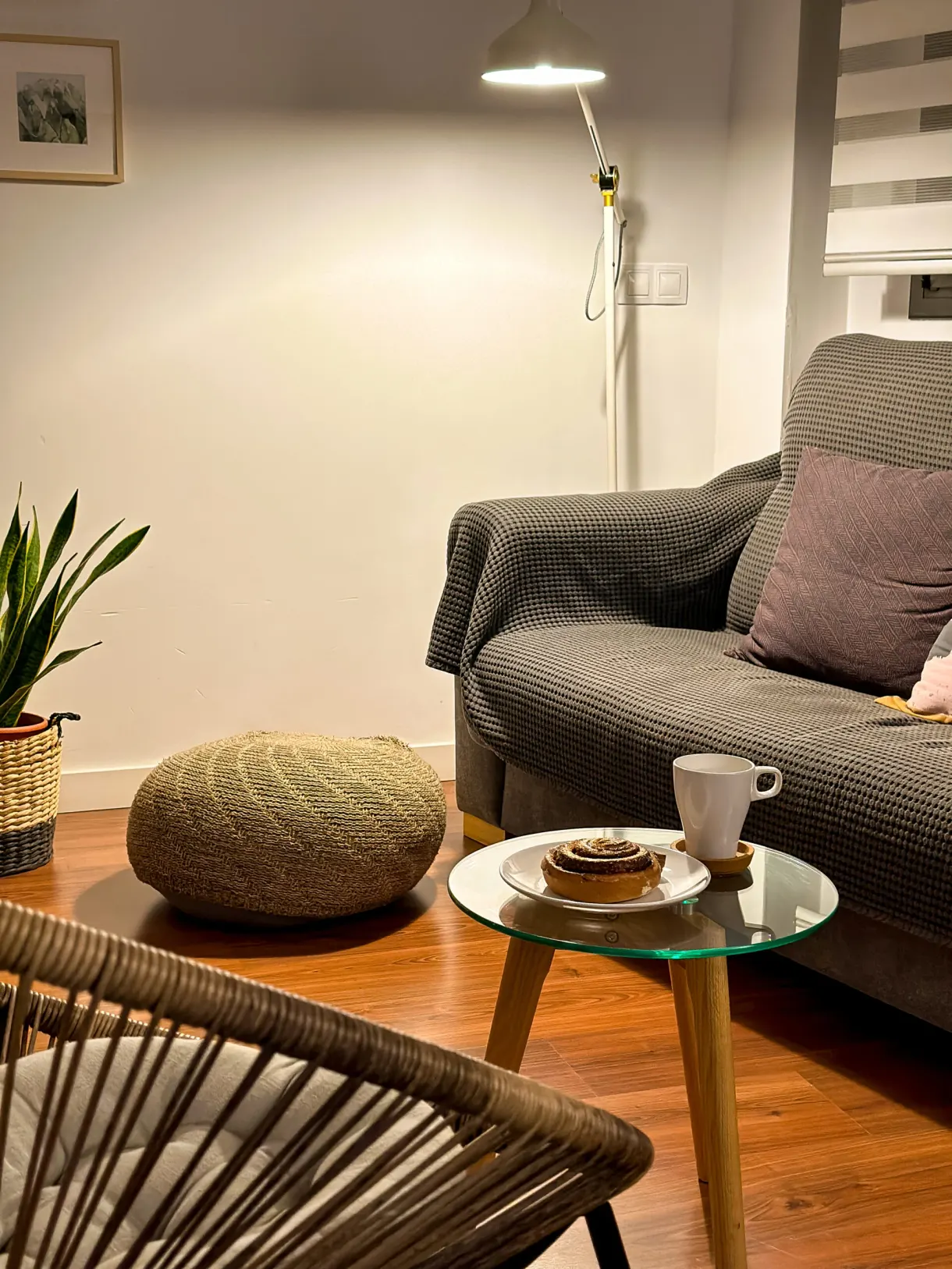 Sitting area with a grey sofa, woven pouffe and coffee served