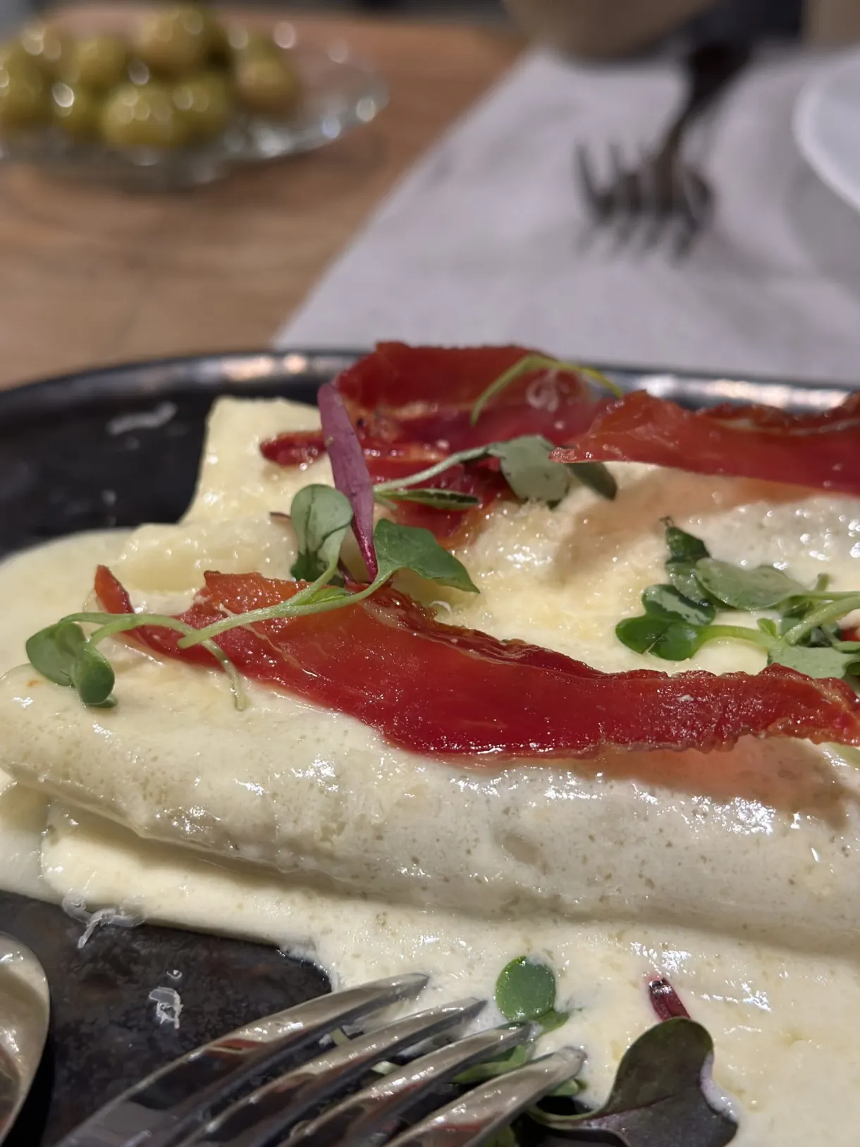 Plate of creamy pasta topped with cured ham and shoots