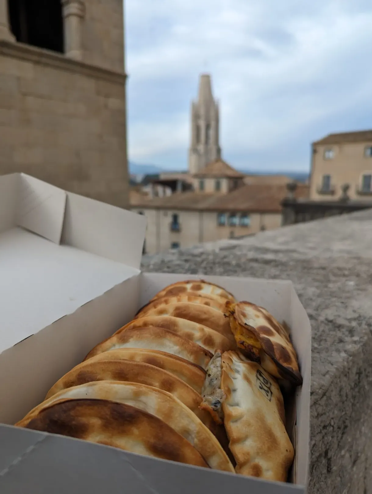 Box of golden empanadas open facing the roofs and the bell tower