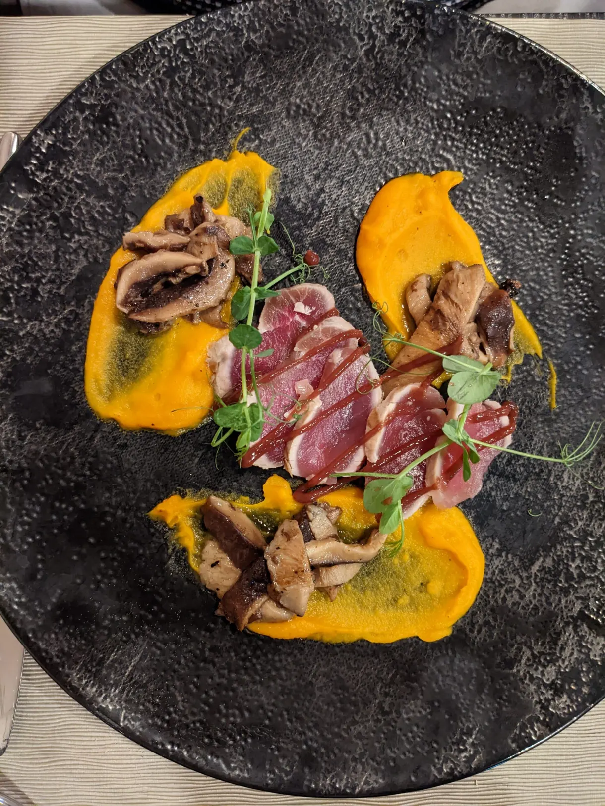 Sliced duck breast on orange purée in a black plate