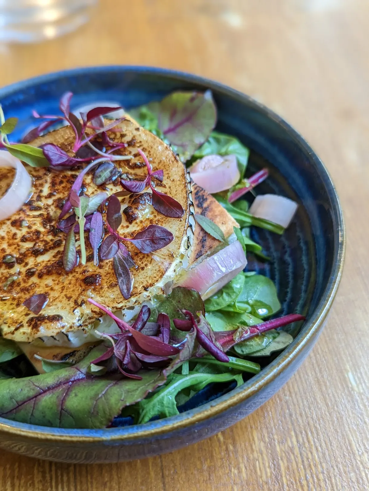 Golden galette and baby greens served in a blue bowl
