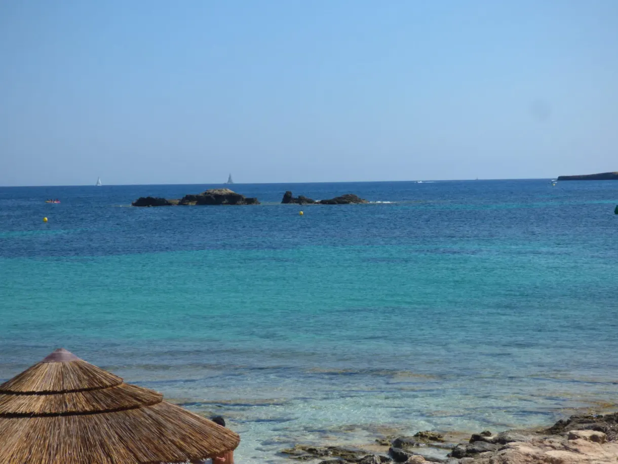 Turquoise sea and islets seen from beneath a straw parasol