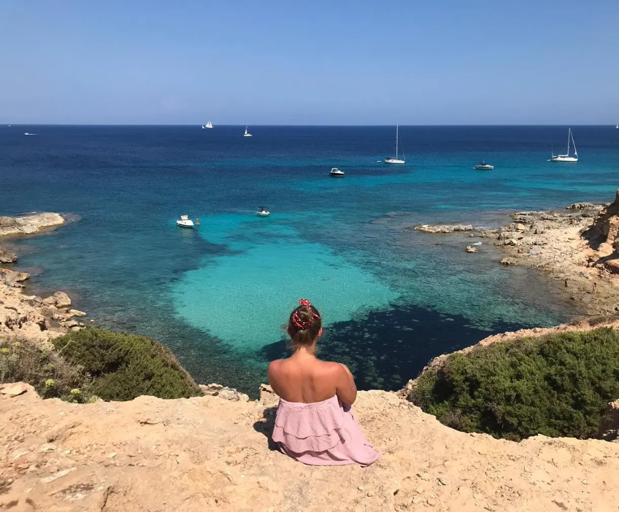 Sitting at the edge of the cliff facing the turquoise cove