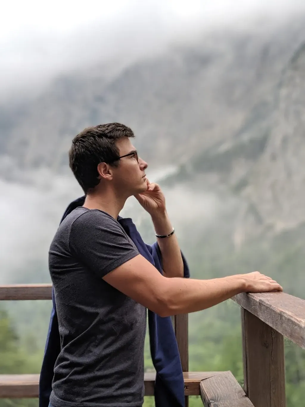 Leaning on a railing facing the misty rock wall