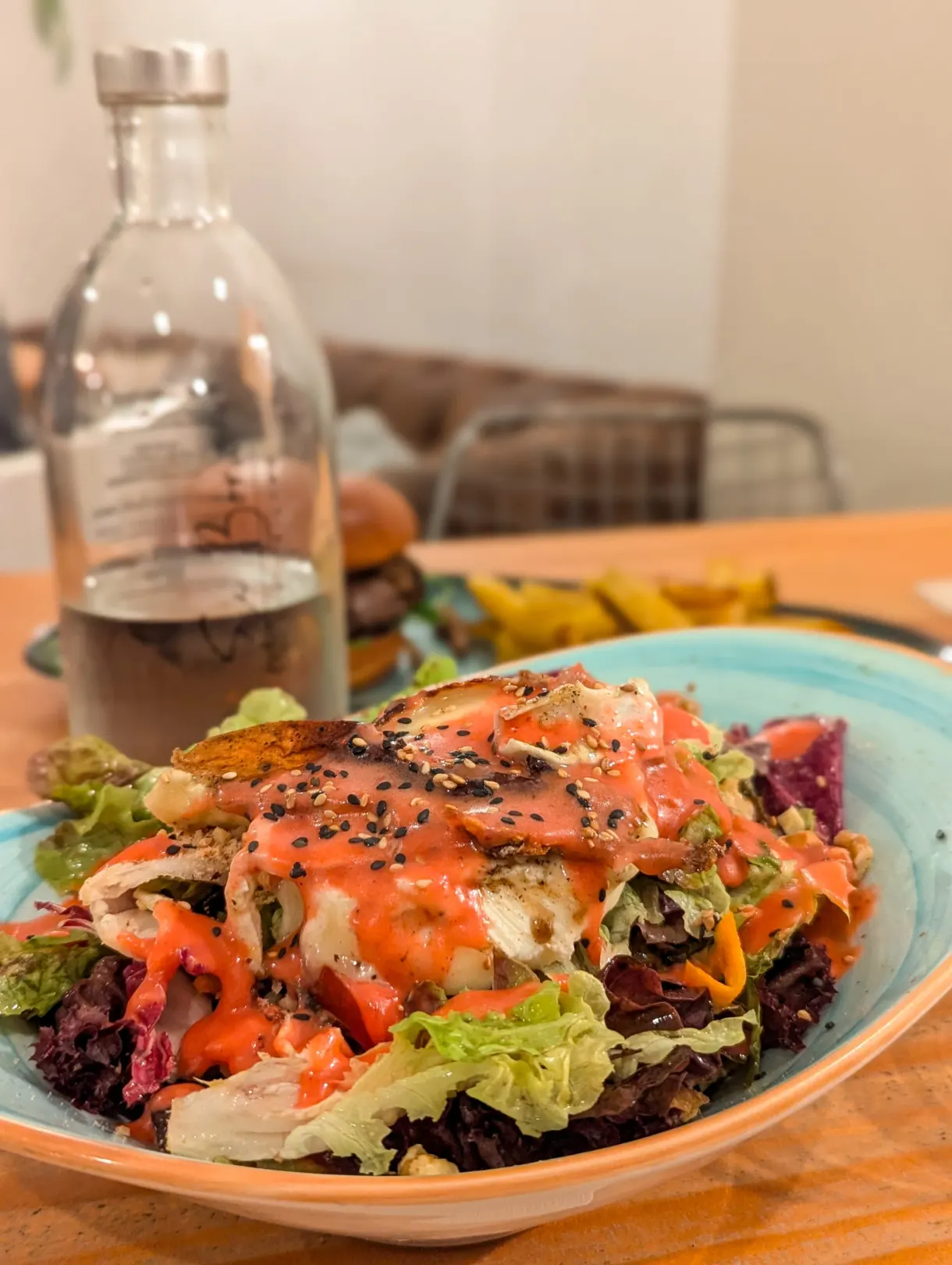 Large salad coated in dressing, carafe of wine behind