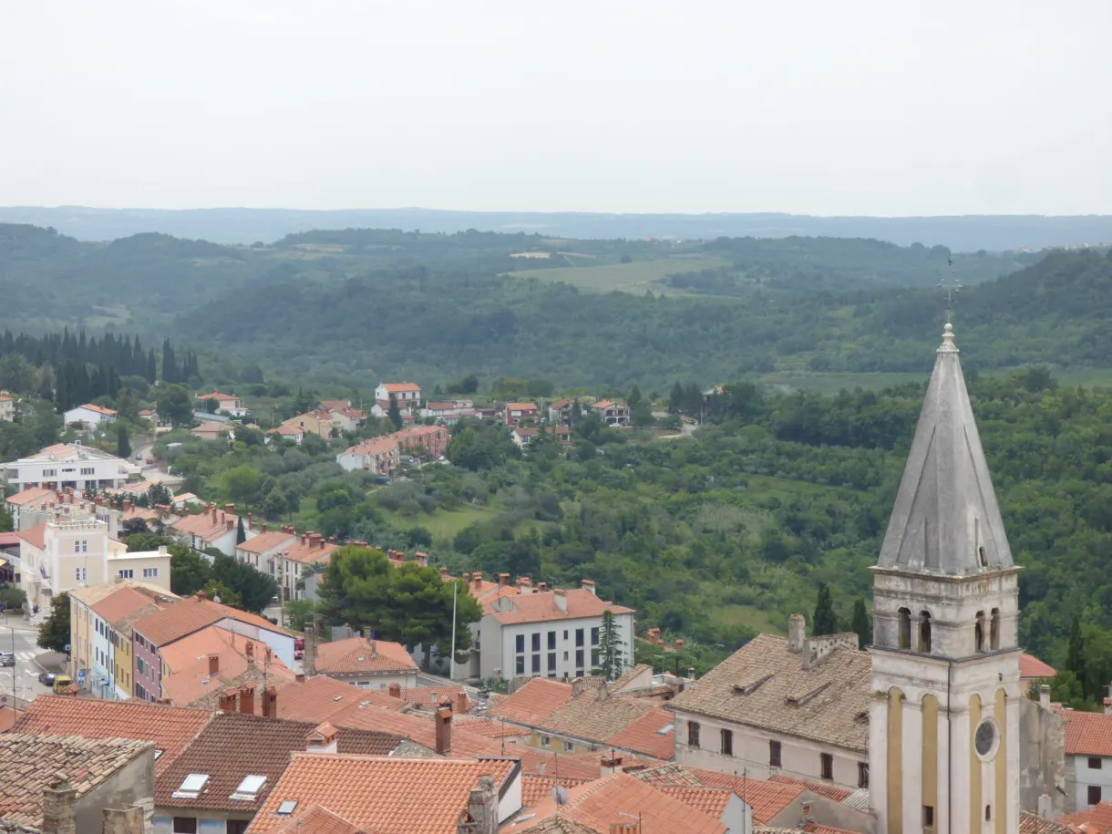 Tiled roofs and pointed bell tower of Buje amid the hills