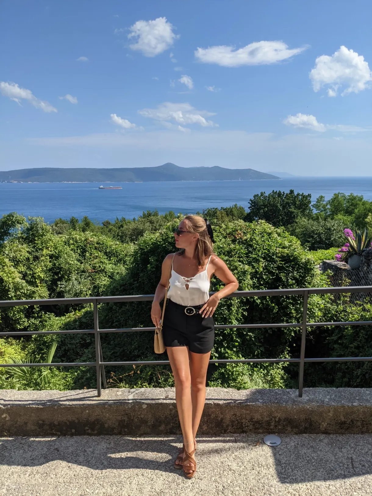 Woman leaning on a railing facing the sea and the distant hills