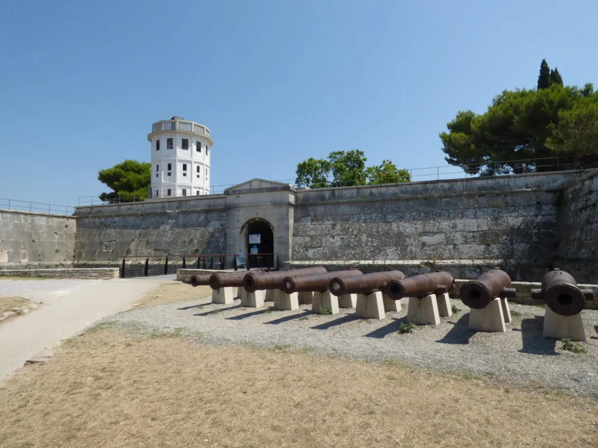 Cannons lined up in front of the rampart and the white tower of the fortress of Pula