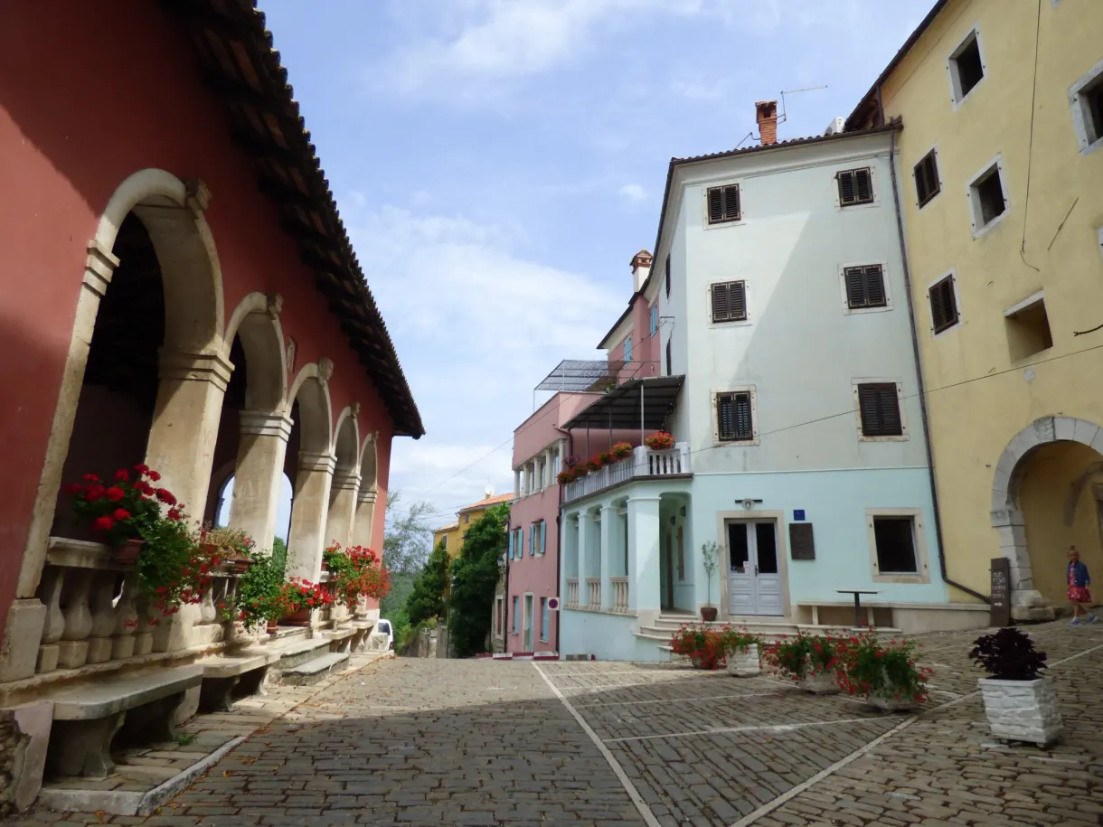 Red arcaded loggia opening onto the cobbled square of Oprtalj