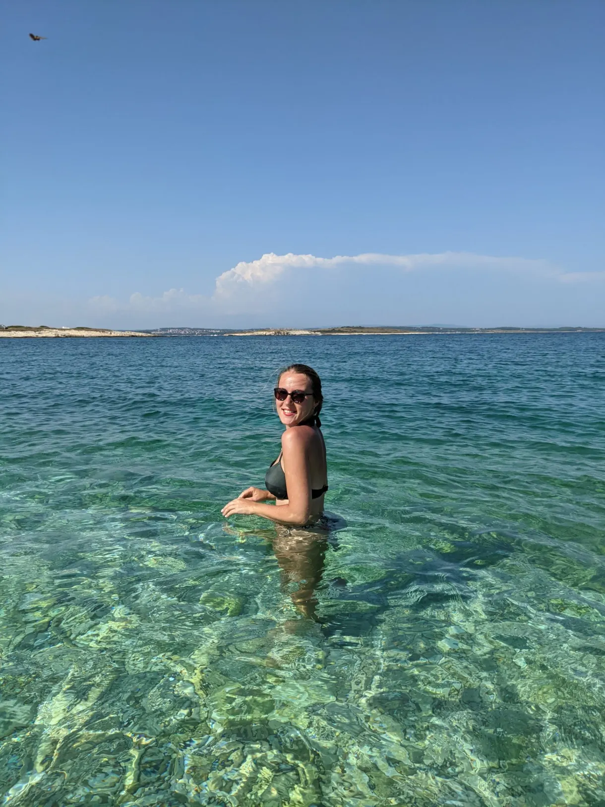 Woman in sunglasses bathing in the clear water of Kamenjak