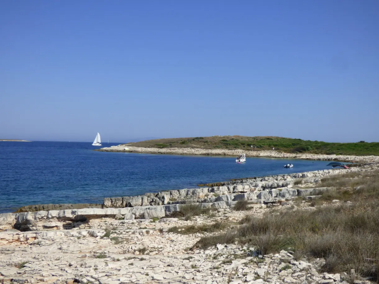 Flat rocky shore of Kamenjak, sailing boat out to sea