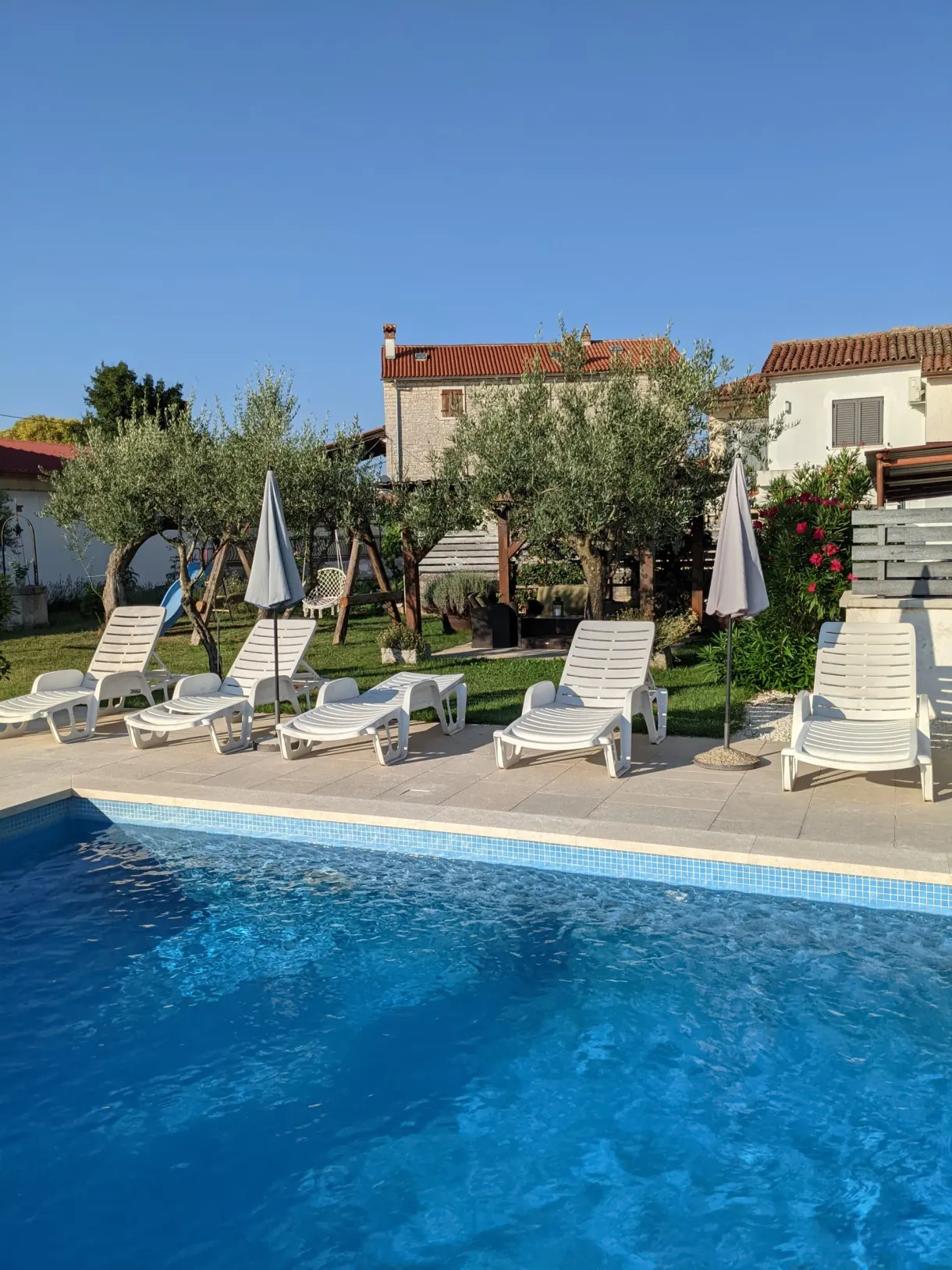 Pool lined with sun loungers and parasols in front of the holiday house