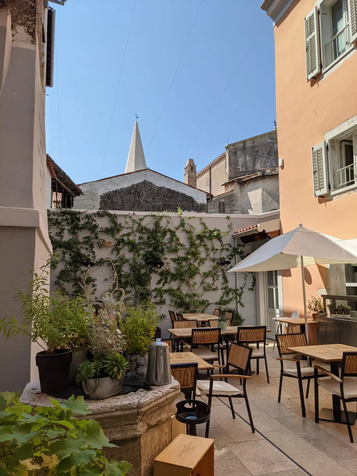 Restaurant courtyard with laid tables and parasol, bell tower in the background