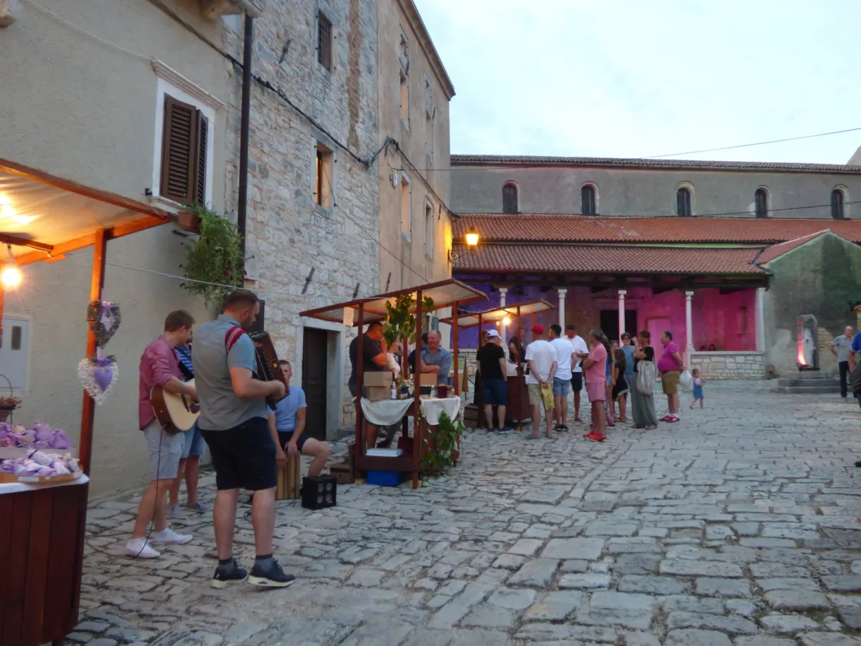 Lit-up stalls and strollers in a street of Sveti Lovreč in the evening