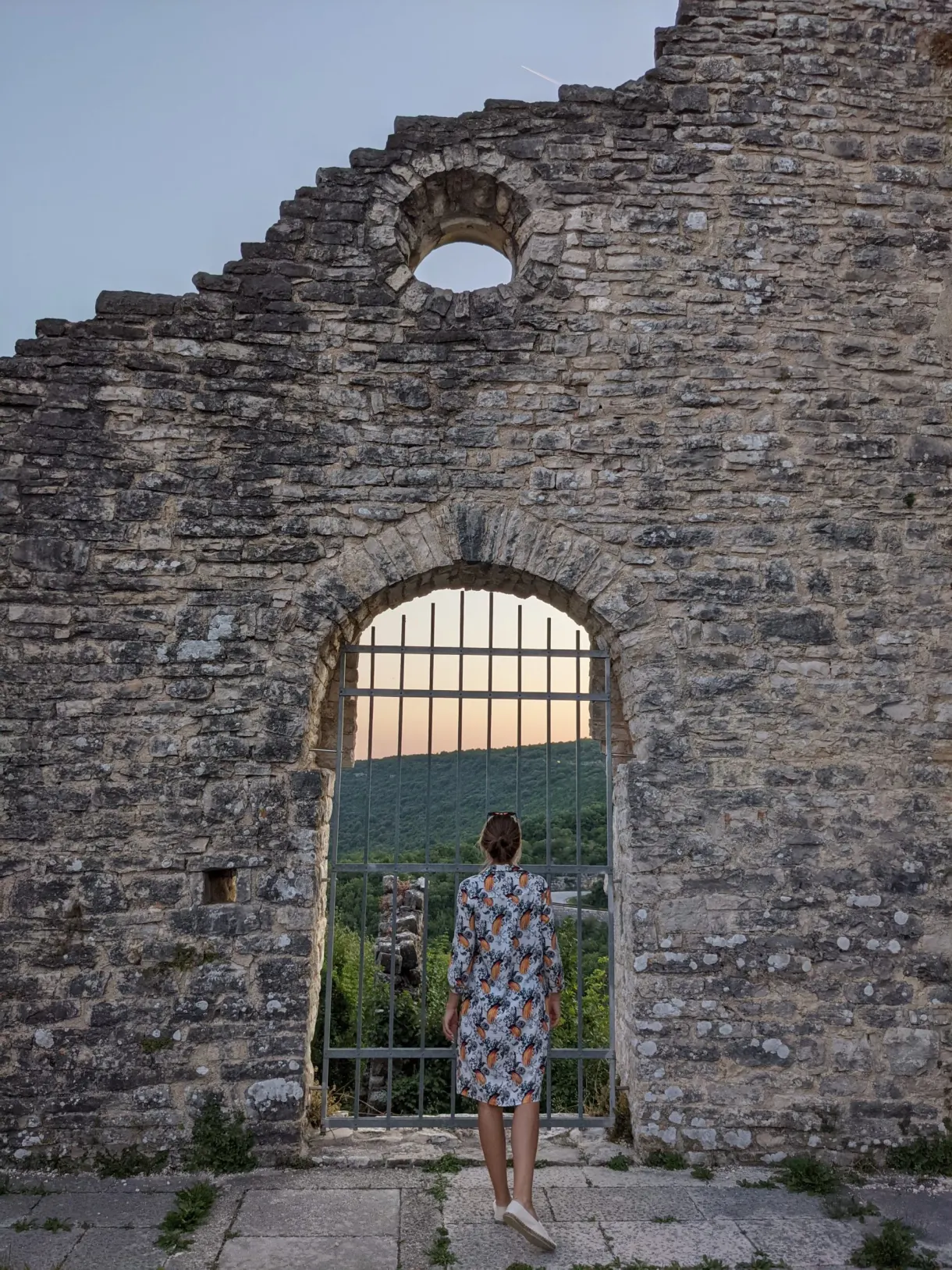 Woman in front of the tall grilled bay of a ruined church in Dvigrad